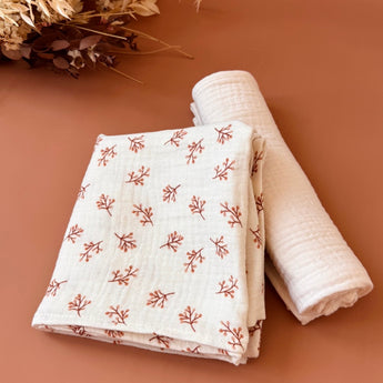 un lot de deux langes pour bébé en double gaze, un de couleur crème et un avec des branches imprimées 